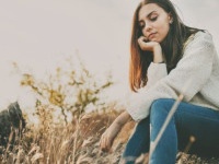 Teenage girl sitting alone on autumn cold day. Lonely sad young woman wearing warm sweater thinking and hesitating. Loneliness and solitude concept.