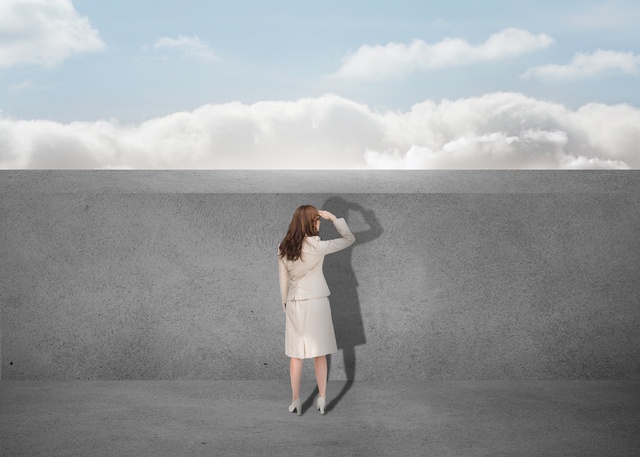 Businesswoman watching a grey wall with the sky in background