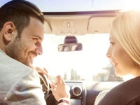 A young woman and a young man are laughing in the car, enjoying in the road trip. The man is driving.