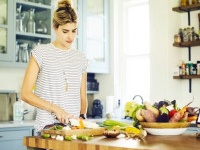 Beautiful woman cutting carrot at kitchen island. She is preparing food at home. Female is in casuals.