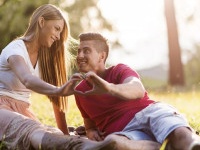 Young happy couple relaxing outdoors while making heart shape with their hands and looking at each other.