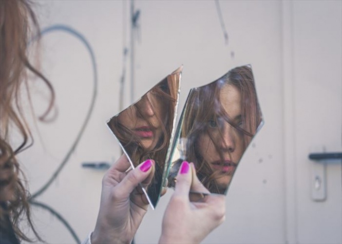 Beautiful redhead girl with long hair and blue eyes looking at herself in a broken mirror