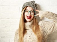 Funny Hipster Girl in Knitted Sweater and Beanie Hat Going Crazy at White Brick Wall Background. Trendy Casual Fashion Outfit in Winter. Toned Photo with Copy Space.