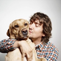 Closeup portrait handsome young hipster man, kissing his good friend dog isolated black grey background. Positive human emotions, facial expression, feelings.