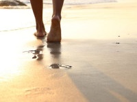 Girl walking on wet sandy beach leaving footprints in the sand at sunset time