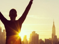Instagram style filter silhouette of a successful woman or girl arms raised celebrating at sunrise or sunset in front of the New York City Skyline
