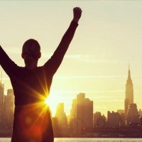 Instagram style filter silhouette of a successful woman or girl arms raised celebrating at sunrise or sunset in front of the New York City Skyline