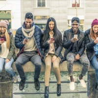 Multicultural group of friends using cellphones - Students sitting in a row and typing on the smartphones