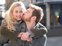 Loving young couple outdoors on the street kissing and man carrying woman on a piggyback ride