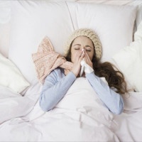 Sick woman with thermometer is lying in bed. She has cold, flu and high fever.