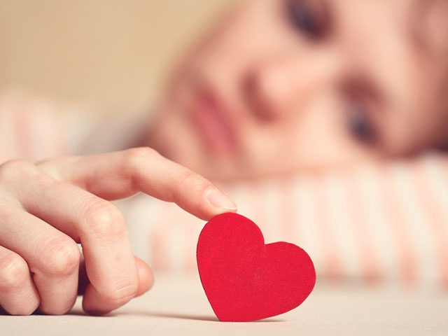 Sad girl is holding heart symbol by her finger