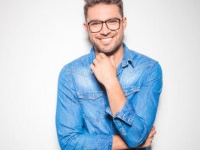 beautiful young man wearing glasses, smiling and touching his chin