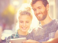 Smiling couple taking selfie through smart phone. Male and female partners spending leisure time in city. They are wearing casuals on sunny day.