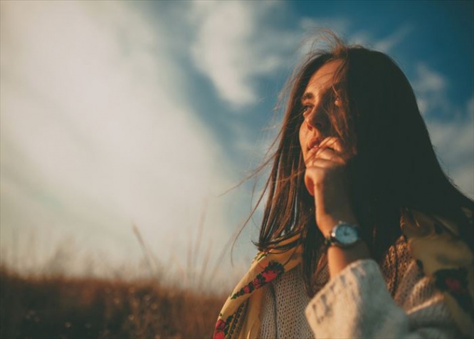 Closeup teenage girl looking into the distance on autumn cold windy day. Handsome young woman wearing warm sweater thinking and hesitating on sky background.