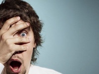 Closeup portrait of handsome young man looking shocked, surprised in disbelief, with hands on face looking at you camera, isolated on background. Positive human emotions, facial expressions