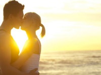 Couple kissing on the beach at sunrise with the sun shining between them