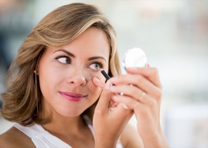 Beautiful portrait of a woman applying eyeliner and looking in a compact mirror - makeup concepts