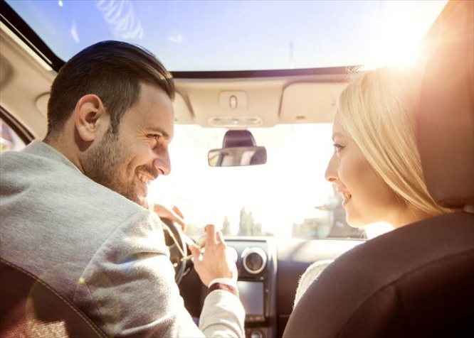 A young woman and a young man are laughing in the car, enjoying in the road trip. The man is driving.