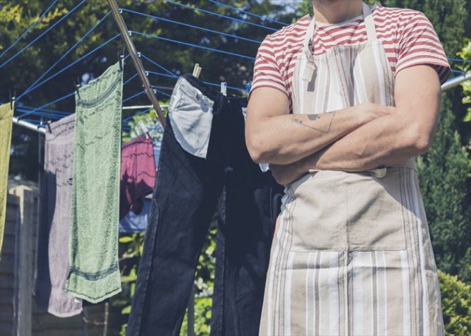 A young man wearing an apron is standing by a clothes line in the garden