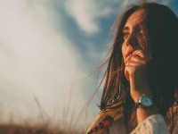 Closeup teenage girl looking into the distance on autumn cold windy day. Handsome young woman wearing warm sweater thinking and hesitating on sky background.