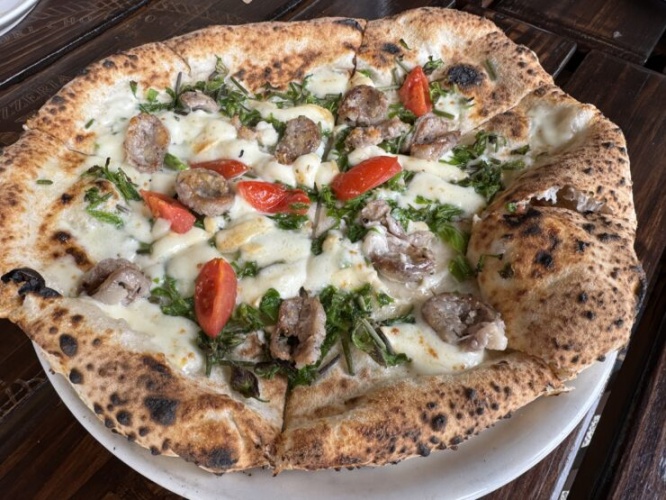 Pizza topped with sausage, cherry tomatoes, herbs and melted cheese on a wood table crust.