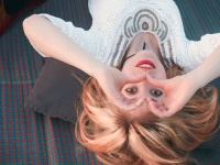 Beautiful girl lying on a mat view upside down, smiling and looking through her hands in the shape of a heart.