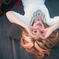 Beautiful girl lying on a mat view upside down, smiling and looking through her hands in the shape of a heart.