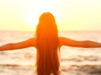 Free woman enjoying freedom feeling happy at beach at sunset. Beautiful serene relaxing woman in pure happiness and elated enjoyment with arms raised outstretched up. Asian Caucasian female model.