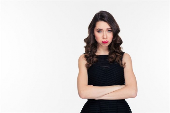 Cute offended sad curly girl with bright makeup in retro style standing with arms crossed over white background