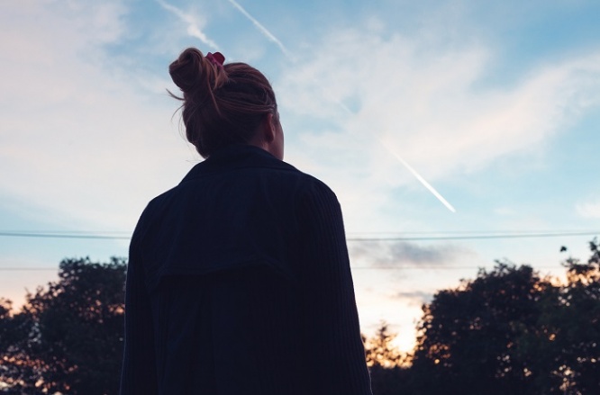 The silhouette of a young woman looking at sunset in the distance.