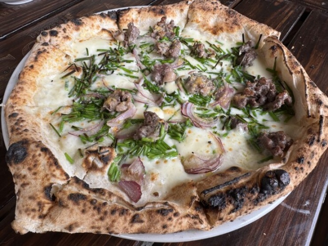 Pizza topped with beef, green onions, and red onions on a lightly charred crust served on a wooden table.