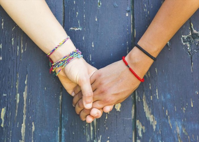 Two women holding hands with a wooden background. One is caucasian, the other is black. Multicultural, homosexual love and friendship concepts.