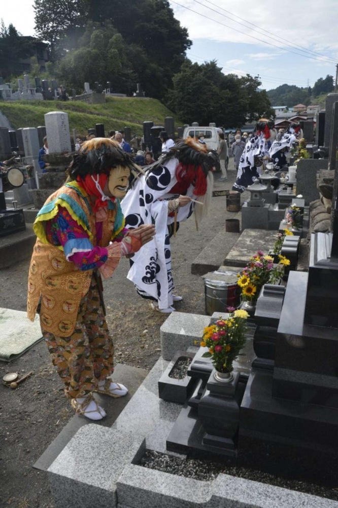 お墓の前で手を合わせる先導役（手前）と獅子役（奥）（画像提供：平川市）