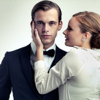 A cropped studio portrait of a dapper young man with a beautiful girl on his arm