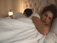 Worried young woman lying in bed away from her boyfriend.