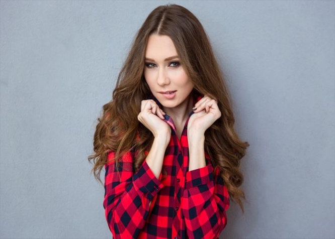 Portrait of a beautiful young woman with curly hair in plaid shirt biting her lips