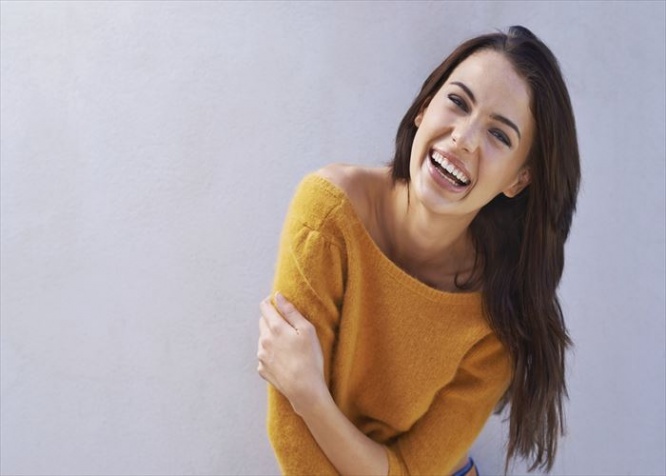 Portrait of a beautiful young woman laughing while standing against a gray wall