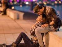 Loving couple relaxing on a riverside during the night while man is kissing his girlfriend on a forehead.