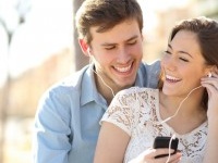 Couple listening to the music with earbuds from a smart phone in a park with an urban background