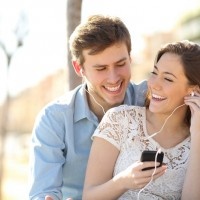Couple listening to the music with earbuds from a smart phone in a park with an urban background