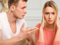 Bad time. Young frowning woman covering her ears while boyfriend is explaining something to her.