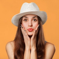 Surprised happy beautiful woman looking sideways in excitement. Excited girl in hat, isolated on orange background