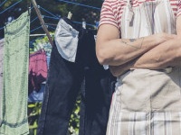 A young man wearing an apron is standing by a clothes line in the garden