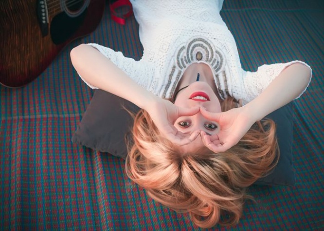 Beautiful girl lying on a mat view upside down, smiling and looking through her hands in the shape of a heart.