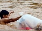 学校に通わせるため、子どもを袋に入れて濁流の川と闘う父親。