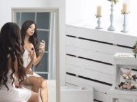 Young beautiful brunette woman sitting against mirror and applying perfume