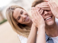 Woman surprising her boyfriend outdoors and covering his eyes - relationship concepts