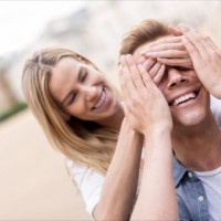 Woman surprising her boyfriend outdoors and covering his eyes - relationship concepts