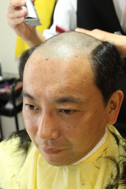 男性用かつらを体験するために髪を剃る記者