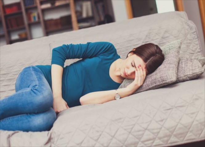Young woman in pain, lying down on the couch in the living room